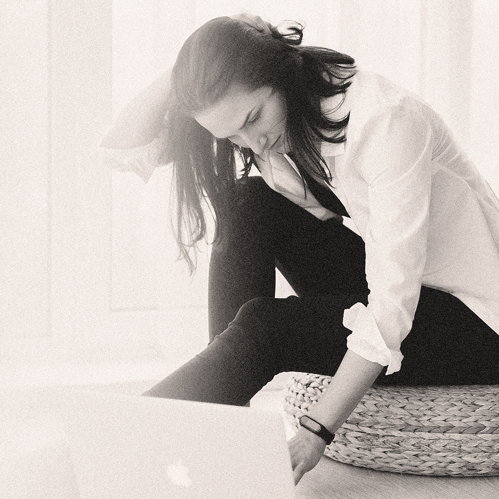 Woman sitting in a minimal space, looking down thoughtfully, representing reflection and brand alignment